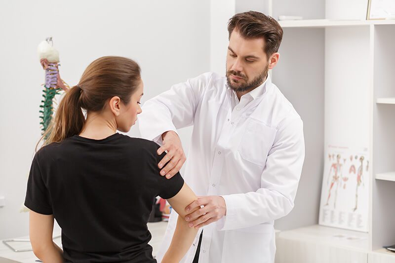ACG Male doctor examining female patient suffering from elbow pain