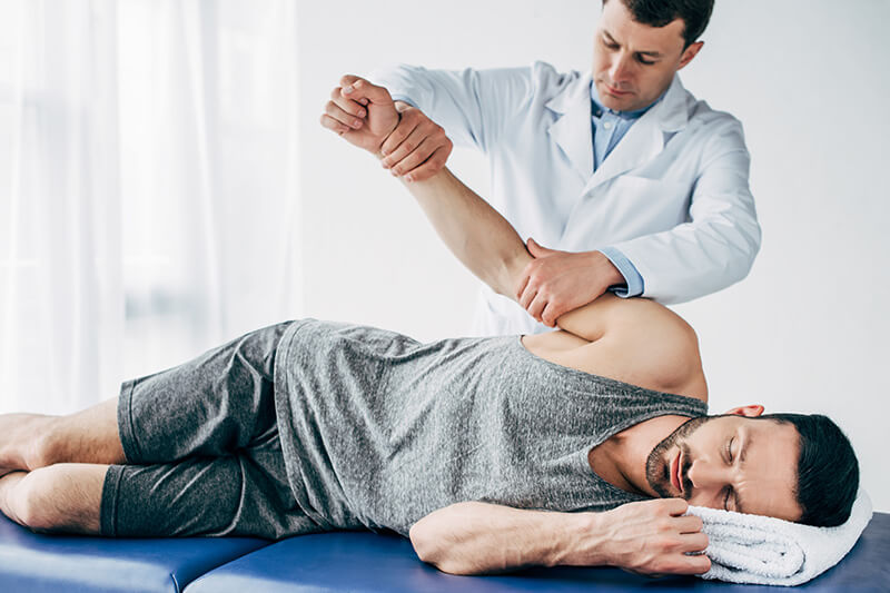 ACG chiropractor stretching arm of handsome patient lying on massage table in hospital